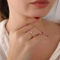 Close-up of a hand wearing a gold ring with a pink gemstone, blurred background