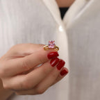 Hand wearing a gold ring with a pink tourmaline gemstone against a white background