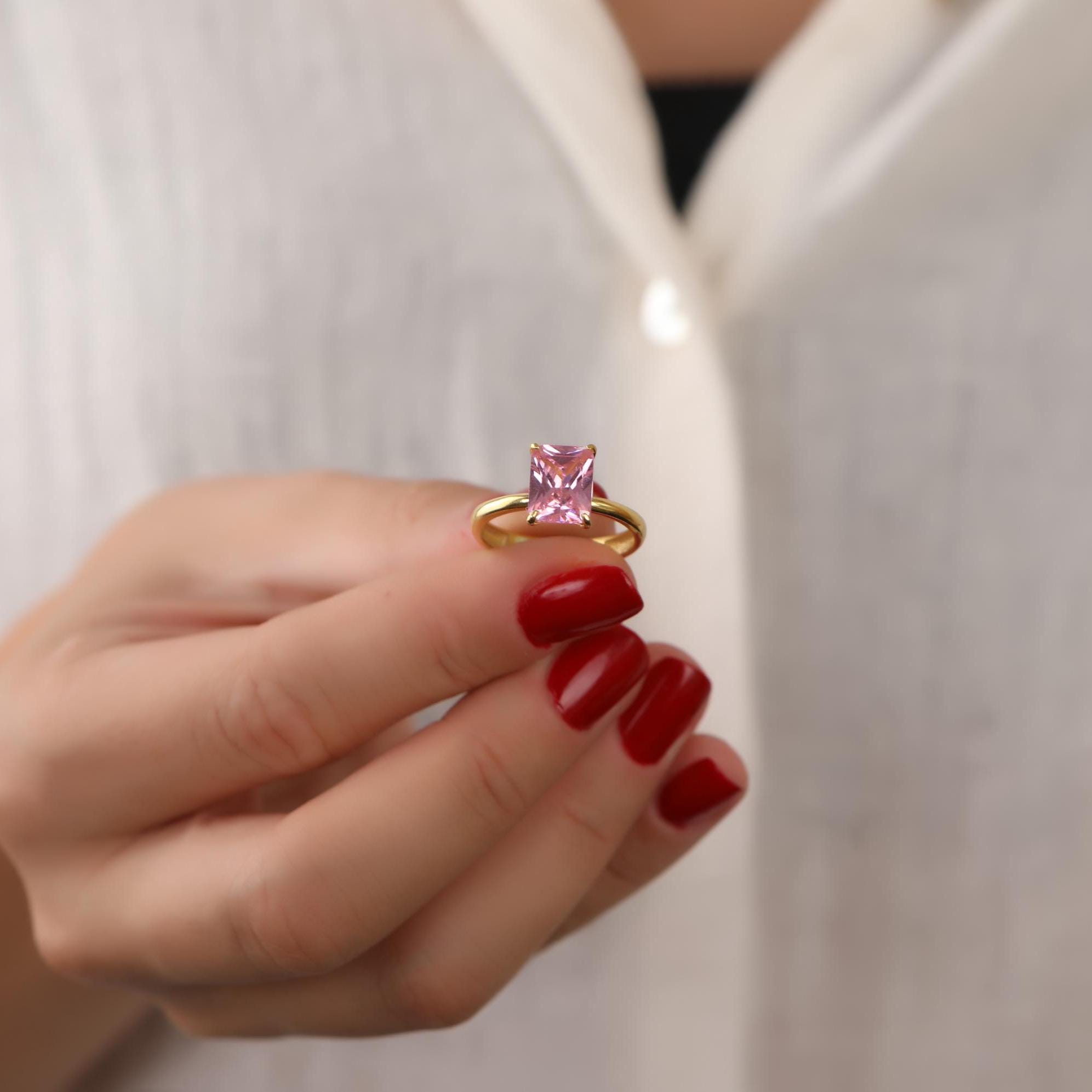 Hand wearing a gold ring with a pink tourmaline gemstone against a white background