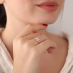 Close-up of a hand wearing a gold ring with a pink gemstone, blurred background