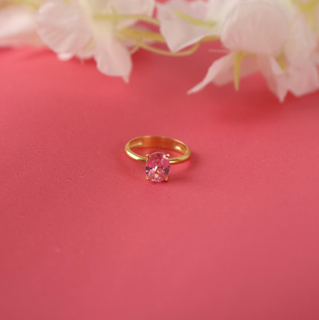 Gold ring with a pink tourmaline gemstone on a pink background with flowers