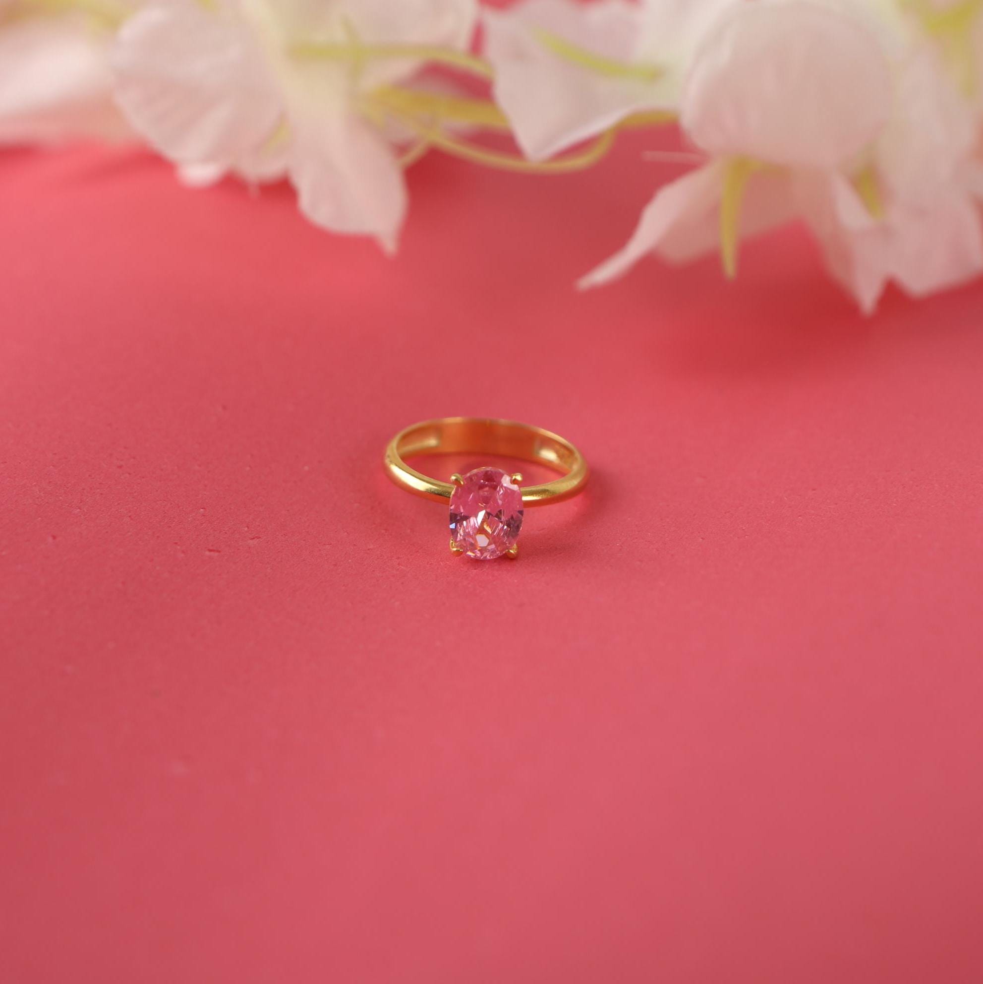 Gold ring with a pink tourmaline gemstone on a pink background with flowers