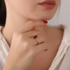 Close-up of a hand wearing a gold ring with a red gemstone, touching the chin.