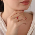 Close-up of a hand wearing a gold ring with a red gemstone, held near the face.