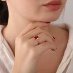 Close-up of a hand wearing a gold ring with a red gemstone, held near the face.