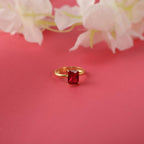 Gold ring with a red gemstone on a pink background with white flowers.