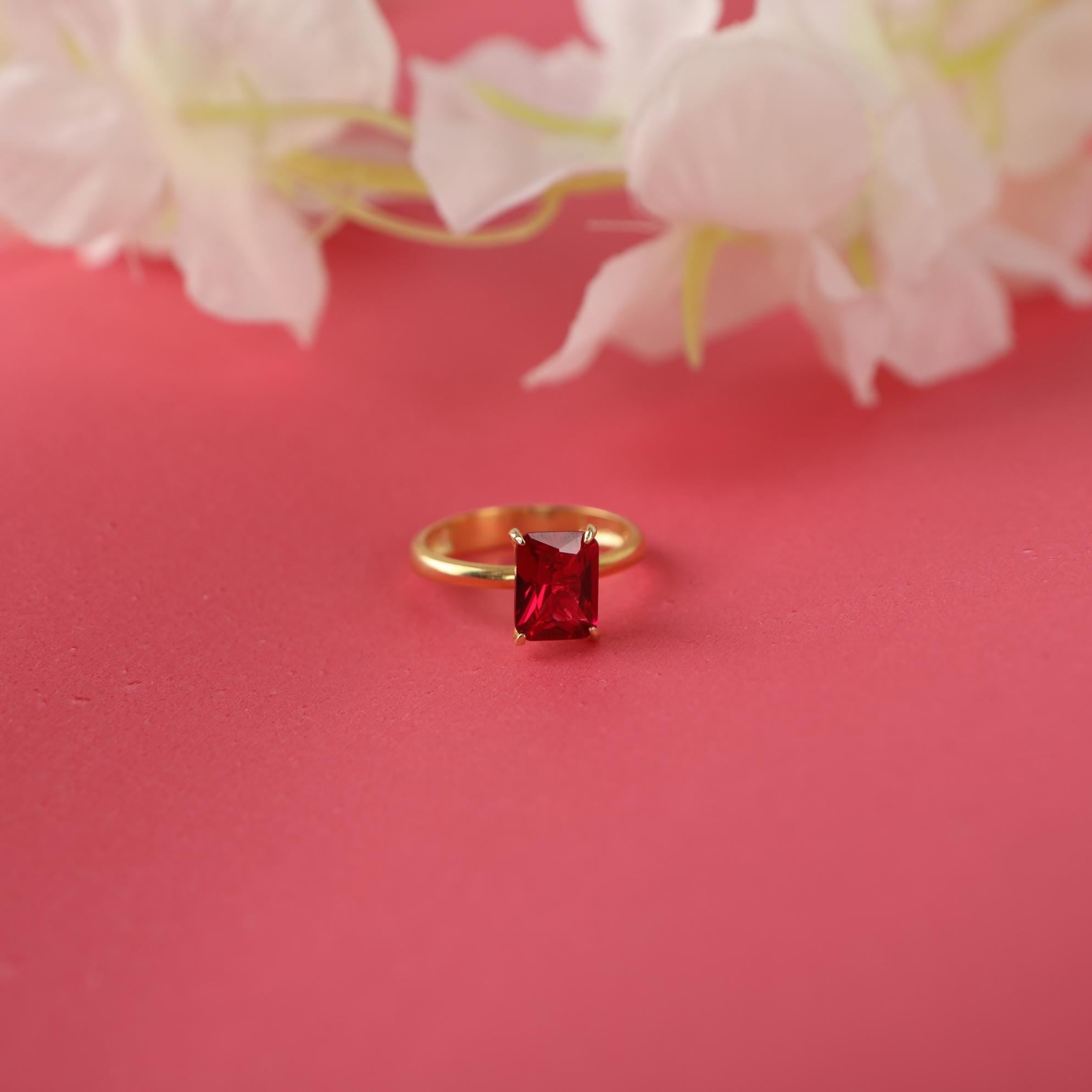 Gold ring with a red gemstone on a pink background with white flowers.