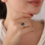 Close-up of a person wearing a gold ring with a blue gemstone, holding their chin.