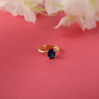 Gold ring with a blue gemstone on a pink background with flowers.