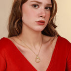 Woman wearing a gold necklace with a circular pendant against a beige background