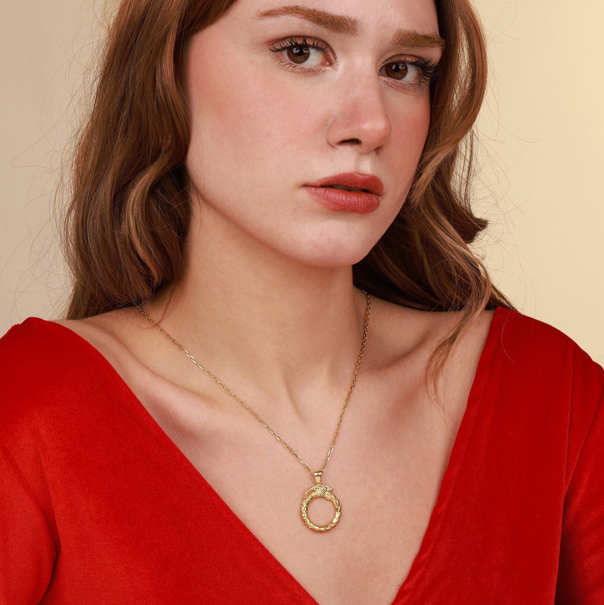Woman wearing a gold necklace with a circular pendant against a beige background