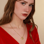 Woman wearing a gold necklace with an origami butterfly pendant against a beige background