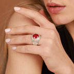Close-up of a hand wearing a ring with a red gemstone on a neutral background
