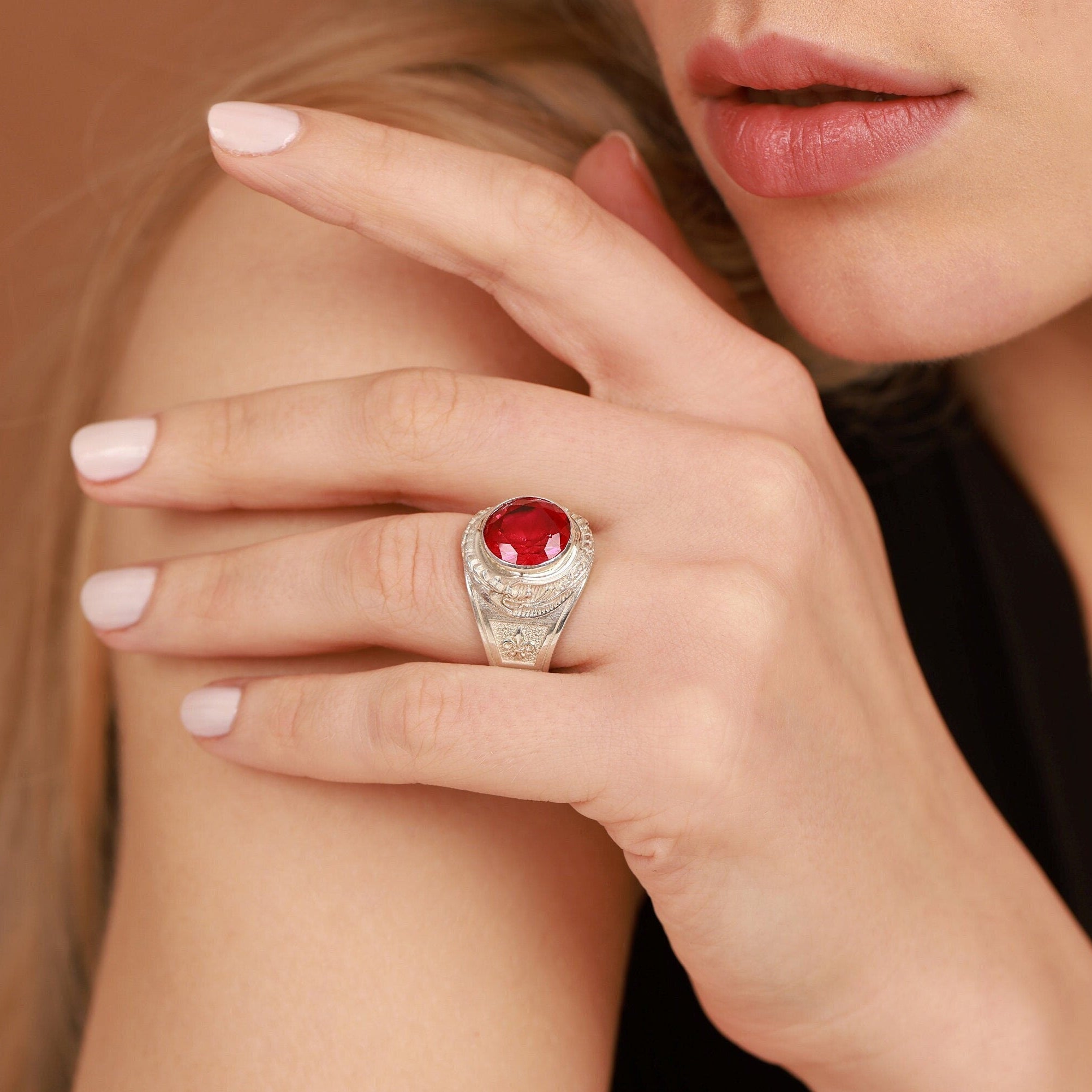 Close-up of a hand wearing a ring with a red gemstone on a neutral background