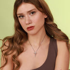 Woman wearing a polished silver necklace with an inri cross pendant against a light green background