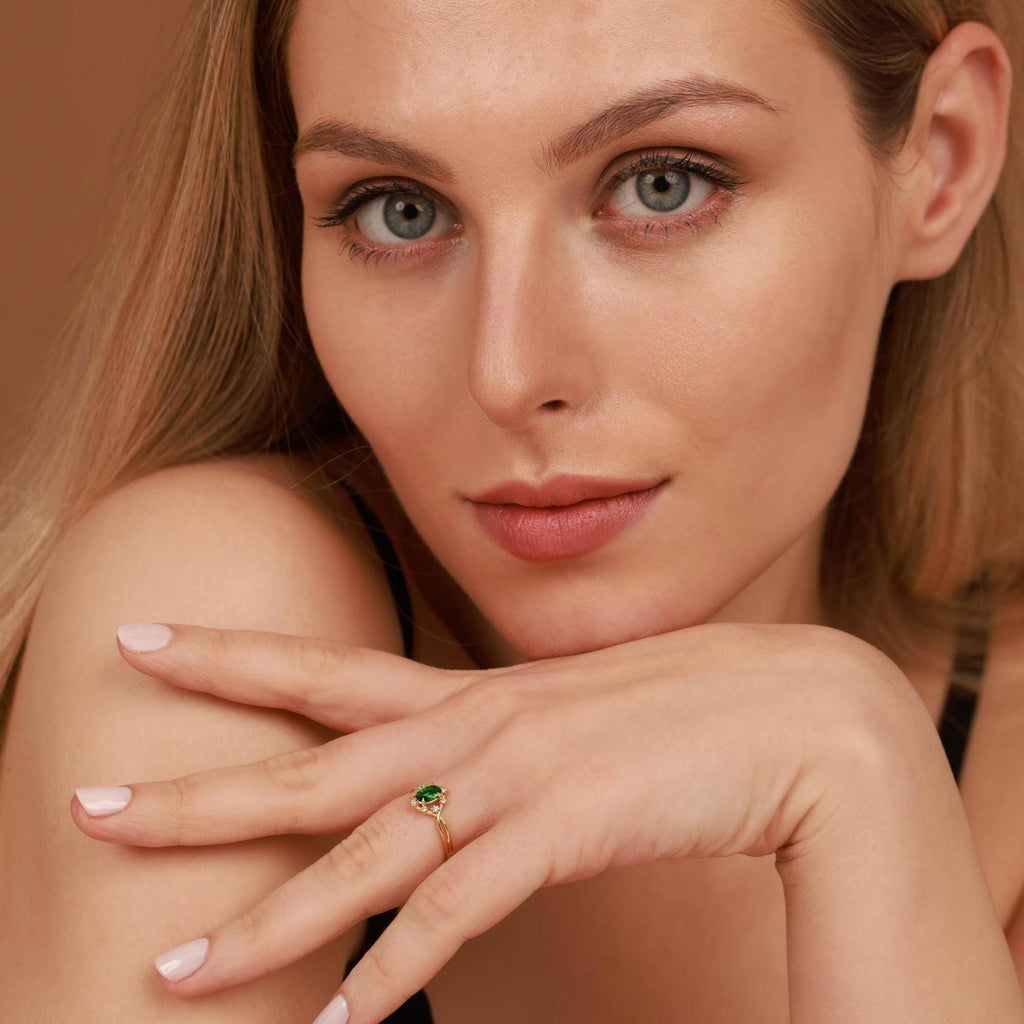 Woman wearing a gold ring with a green emerald gemstone on a neutral background