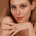 Woman wearing a gold ring with a green emerald gemstone on a neutral background