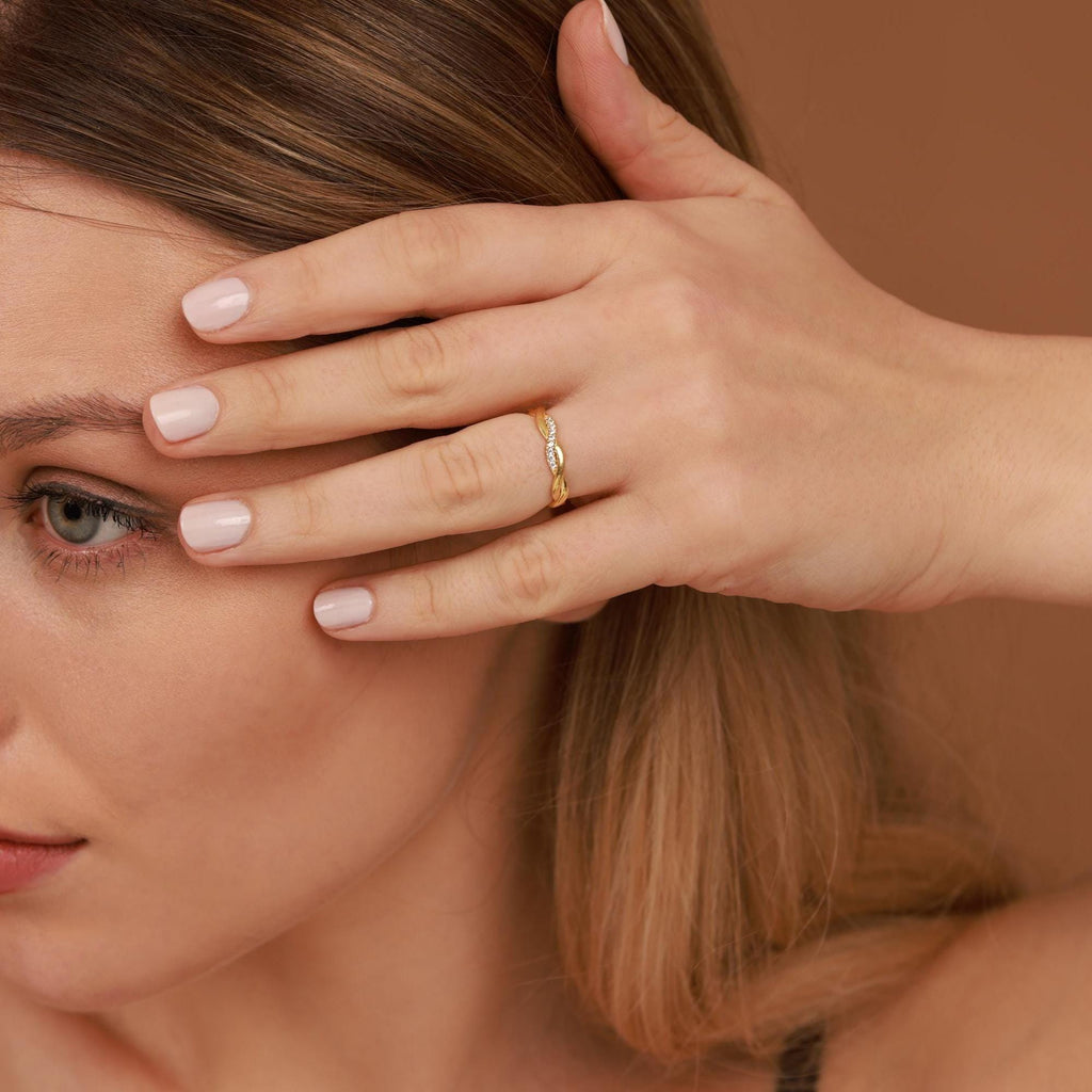 Woman with a gold ring on her finger, holding her hair with her hand against a brown background