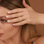 Woman with a gold ring on her finger, holding her hair with her hand against a brown background