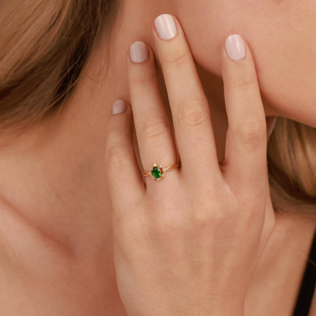 Hand wearing a gold ring with a green gemstone, blurred background