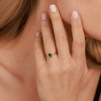Hand wearing a gold ring with a green gemstone, blurred background