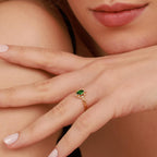 Close-up of a hand wearing a gold engagement ring with a green gemstone.
