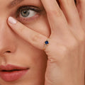 Close-up of a woman wearing a gold ring with a blue gemstone, holding her hand to her face.