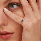 Close-up of a woman wearing a gold ring with a blue gemstone, holding her hand to her face.