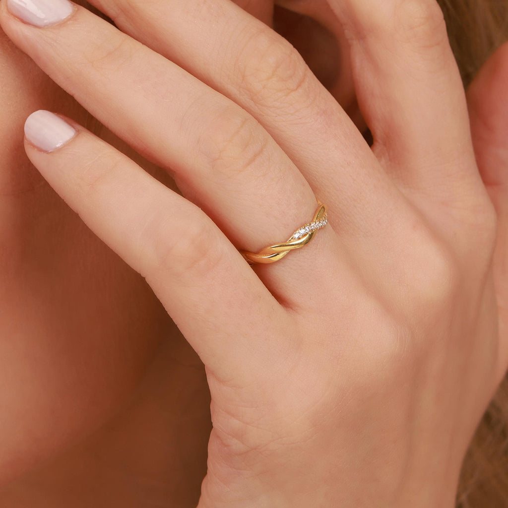 A gold ring with paved small diamonds on a person's finger against a neutral background