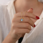 Hand holding a gold necklace with a diamond pendant against a neutral background