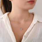 Necklace with a blue gemstone worn by a person in a white shirt.