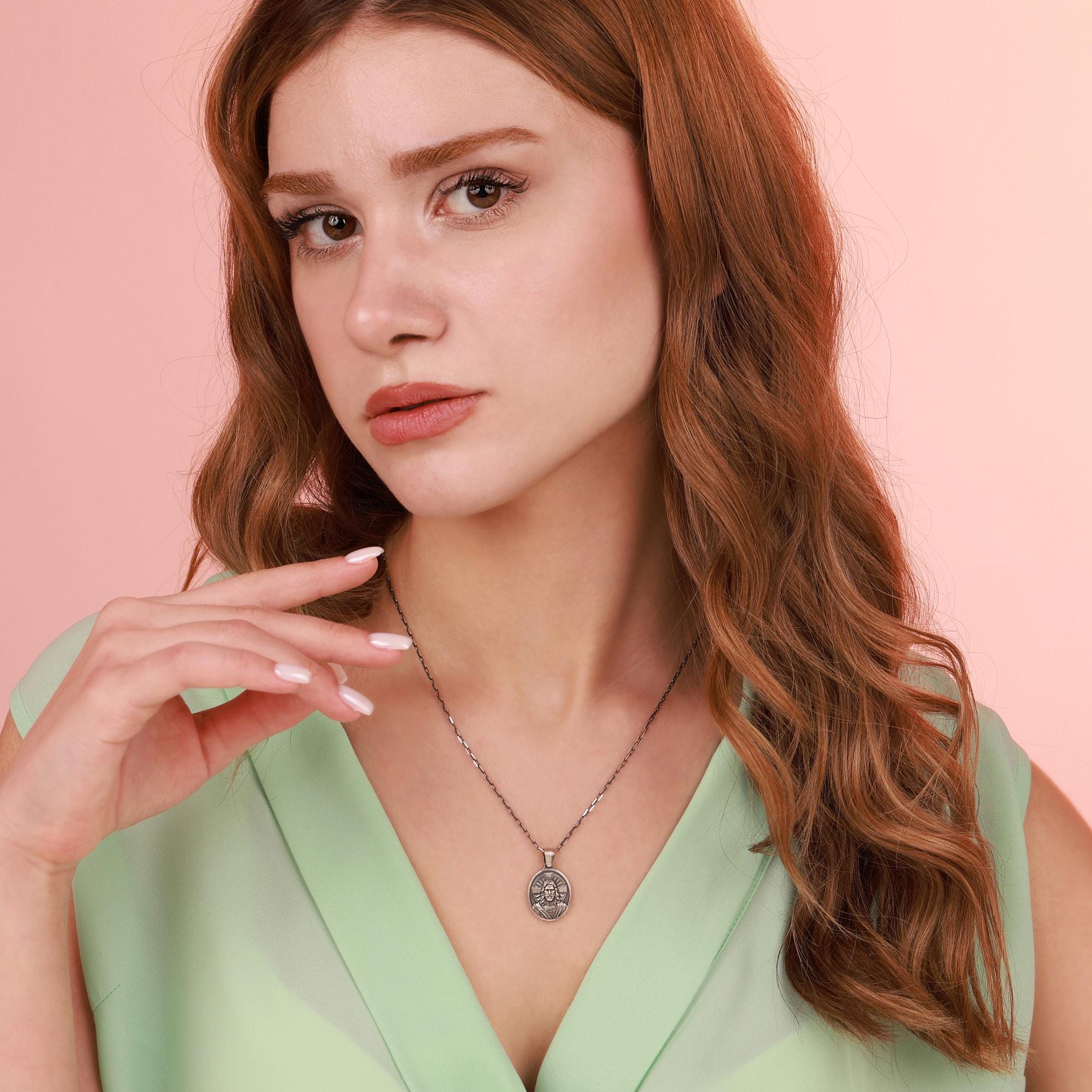 Woman wearing a religious necklace against a pink background