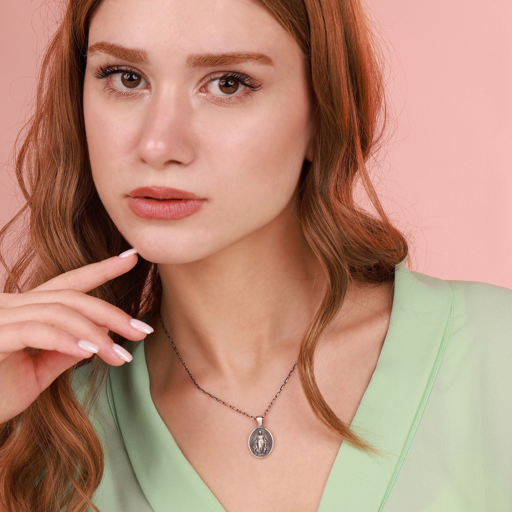 A woman wearing a miraculous necklace with a pink background