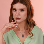 Woman wearing a green top and a necklace with a crown of thorns pendant against a pink background