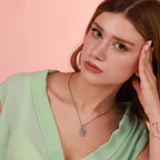 Woman wearing a green top and silver jesus necklace against a pink background