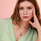 Woman wearing a green top with a sacred heart necklace against a pink background
