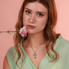 Woman wearing a necklace with an inri cross pendant against a pink background