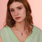 Woman wearing a green top and necklace with a crucifix cross pendant against a pink background