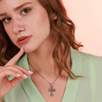 Woman wearing an oxidized sterling silver necklace with an ornate cross pendant against a pink background