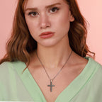 Woman wearing a necklace with a sterling silver flower cross pendant against a pink background