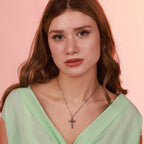 Woman wearing a green top and necklace with a cross formed by interconnected skulls and a coiled snake pendant against a pink background