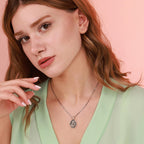 Woman wearing a necklace with an oxidized jesus pendant against a pink background