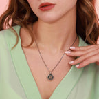 Close-up of a woman wearing a necklace with an oxidized Virgin Mary pendant, against a soft pink background.