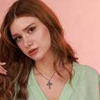Woman wearing a green top and an oxidized silver necklace with a St Michael cross pendant against a pink background