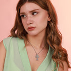 Woman wearing a green top and a sterling silver necklace with a khachkar cross pendant against a pink background