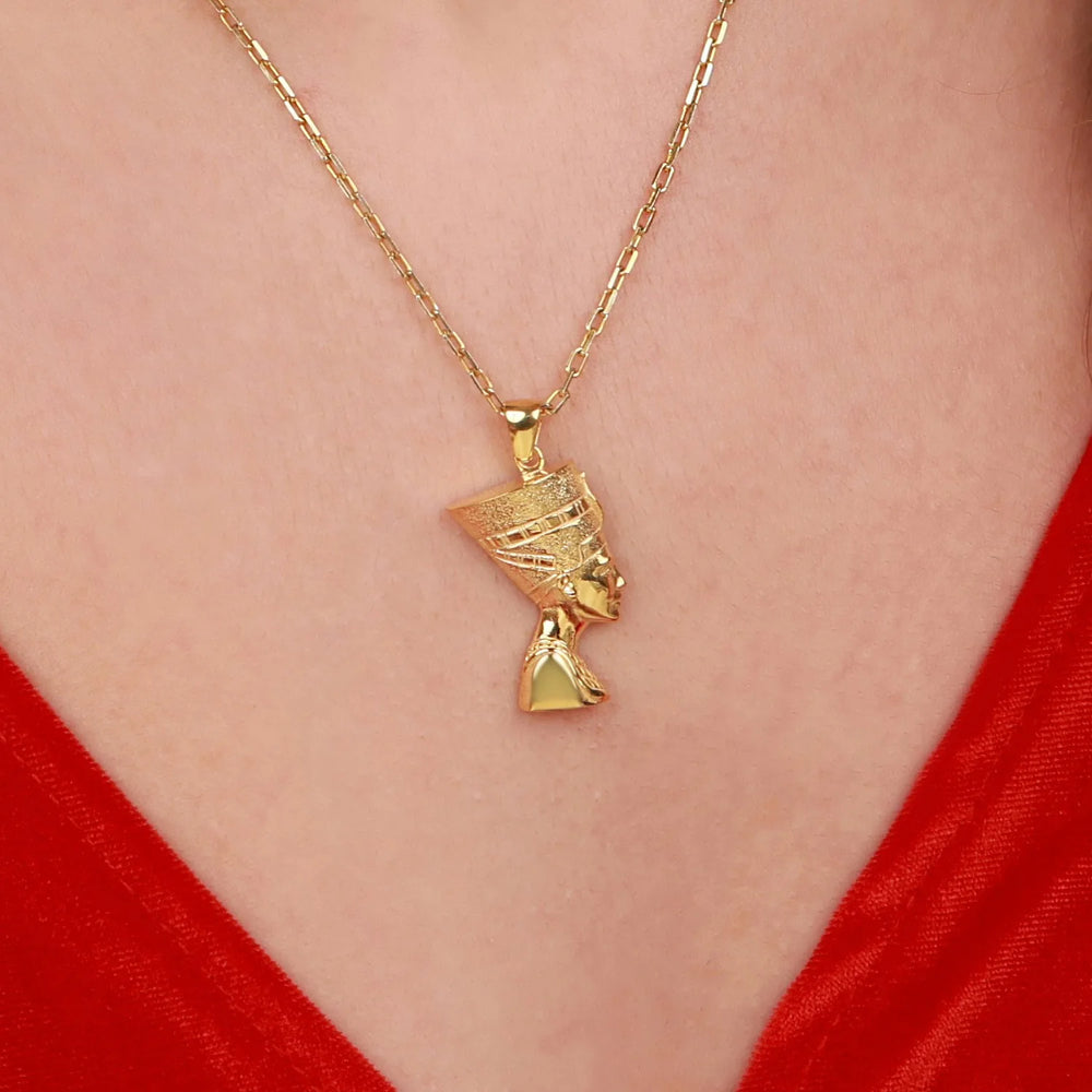 A gold pendant necklace featuring a stylized profile of a woman's head on a delicate chain, shown worn on a person's neck over a red top.