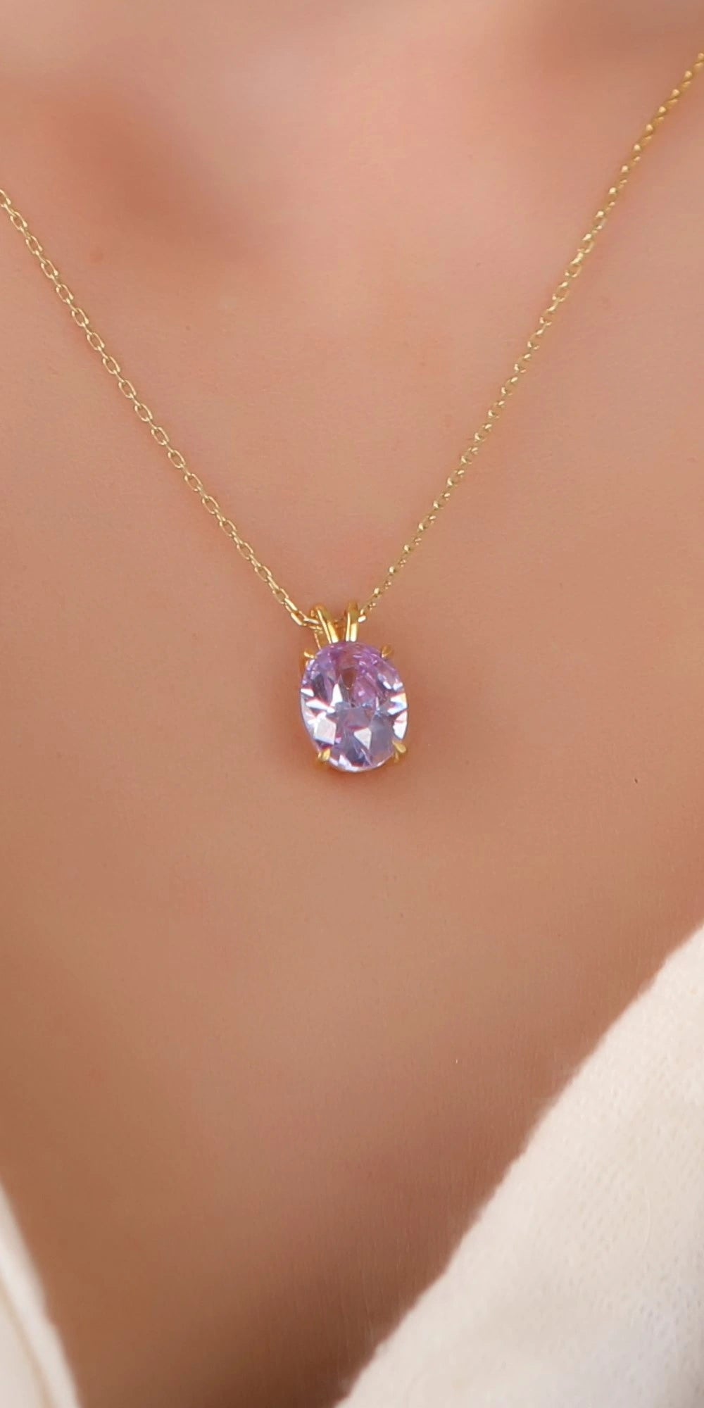 A gold chain necklace with an oval lavender-purple gemstone pendant, worn on a model's neck.