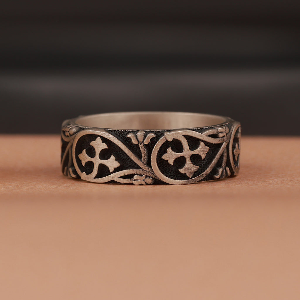 Silver ring with intricate floral designs on a brown surface