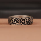 Silver ring with intricate floral designs on a brown surface