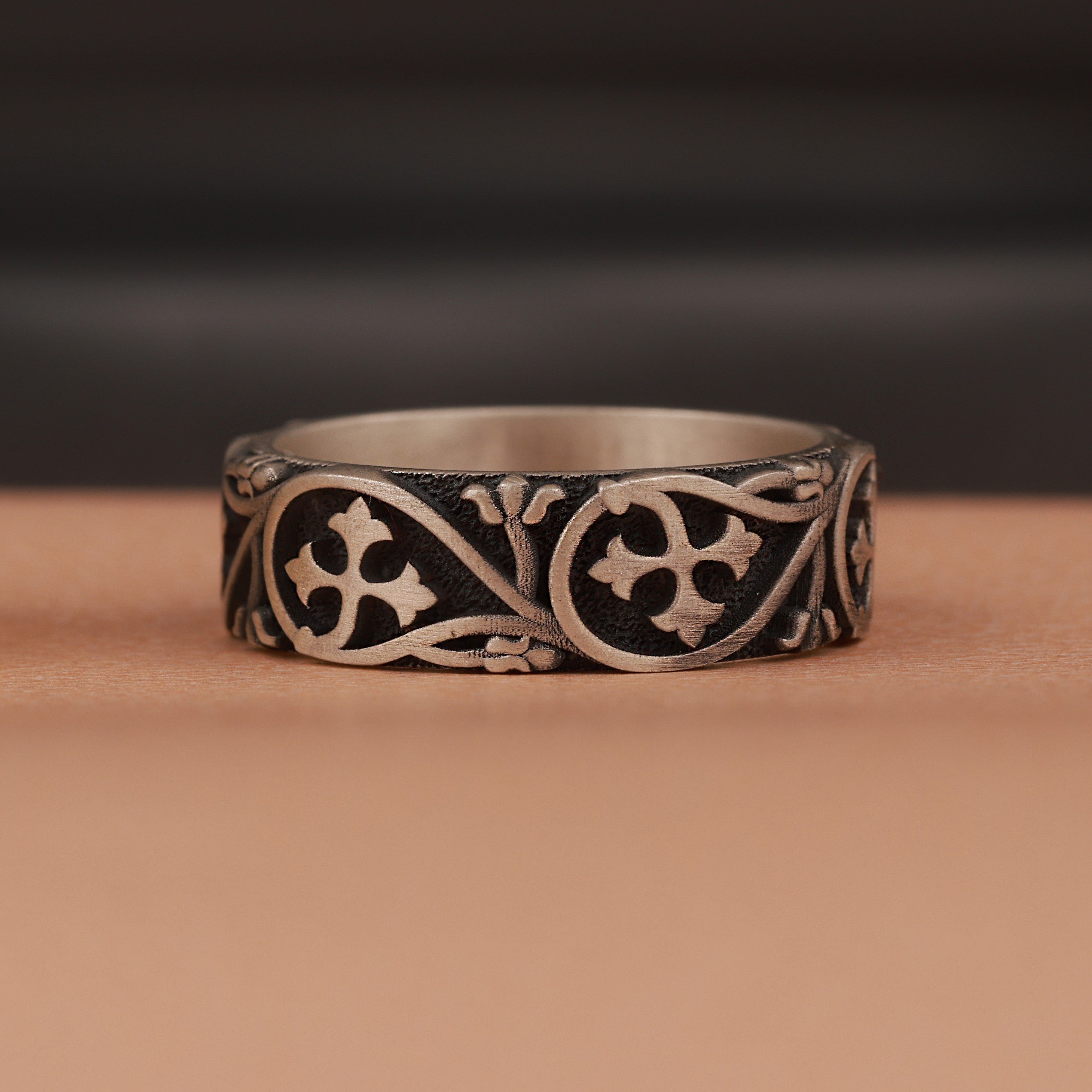 Silver ring with intricate floral designs on a brown surface